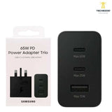 Samsung 65W Trio PD power adapter showing its rectangular UK three-pin wall connection geometry, triple output port configuration panel with dual Type-C slots and single USB-A bay, and robust compact housing